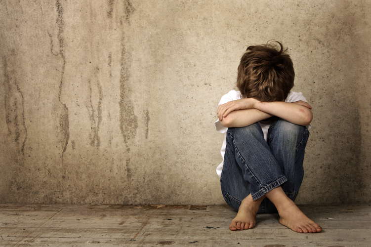 A picture of a boy in the corner of the room, hiding away, upset.